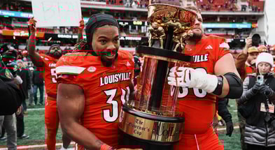 Louisville Cardinals linebacker T.J. Quinn (34) and Louisville Cardinals offensive lineman Pete Nygra (50) carry the Governor's Cup as Louisville Cardinals defensive lineman Clev Lubin (50) held a sign that had BTA written on it as the Cards dominated Kentucky 41-0 Saturday, November 29, 2025 in Louisville, Kentucky at L&N Federal Credit Union Stadium.