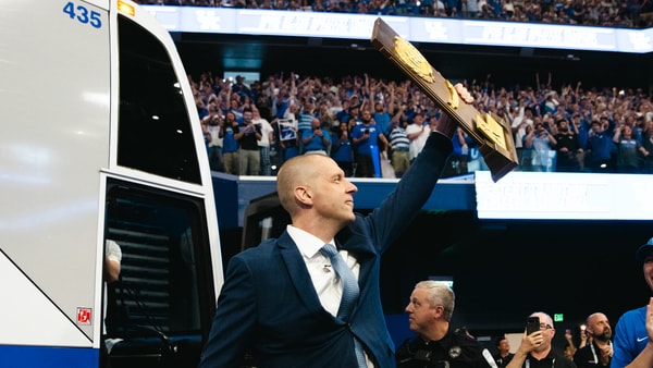 Mark Pope steps off the bus holding the 1996 national championship trophy at his introductory press conference - Aaron Perkins, Kentucky Sports Radio