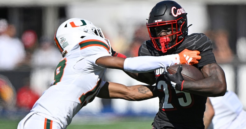 Oct 19, 2024; Louisville, Kentucky, USA; Louisville Cardinals running back Isaac Brown (25) runs the ball against Miami Hurricanes defensive back D'Yoni Hill (19) during the first half at L&N Federal Credit Union Stadium. Mandatory Credit: Jamie Rhodes-Imagn Images