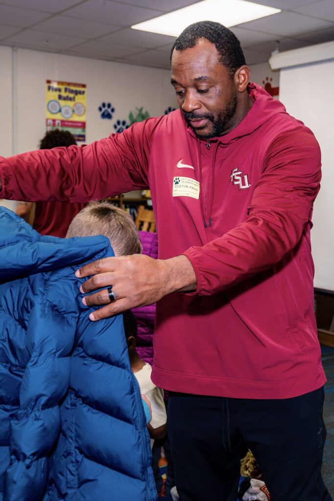 Florida State secondary coach Patrick Surtain helps a student try on a coat donated by the Keep Climbing Family Foundation.